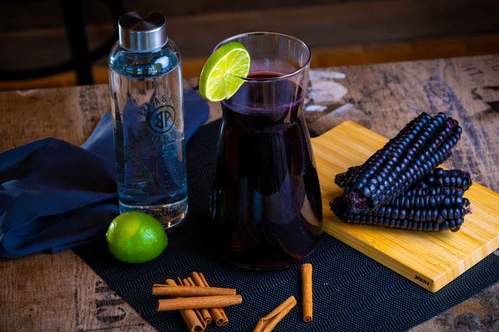 Traditional chicha morada with purple corn, lime, and cinnamon on a rustic table.