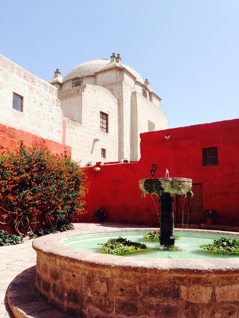 A serene view of the Santa Catalina Monastery courtyard with a water fountain, red walls, and dome in Arequipa, Peru.