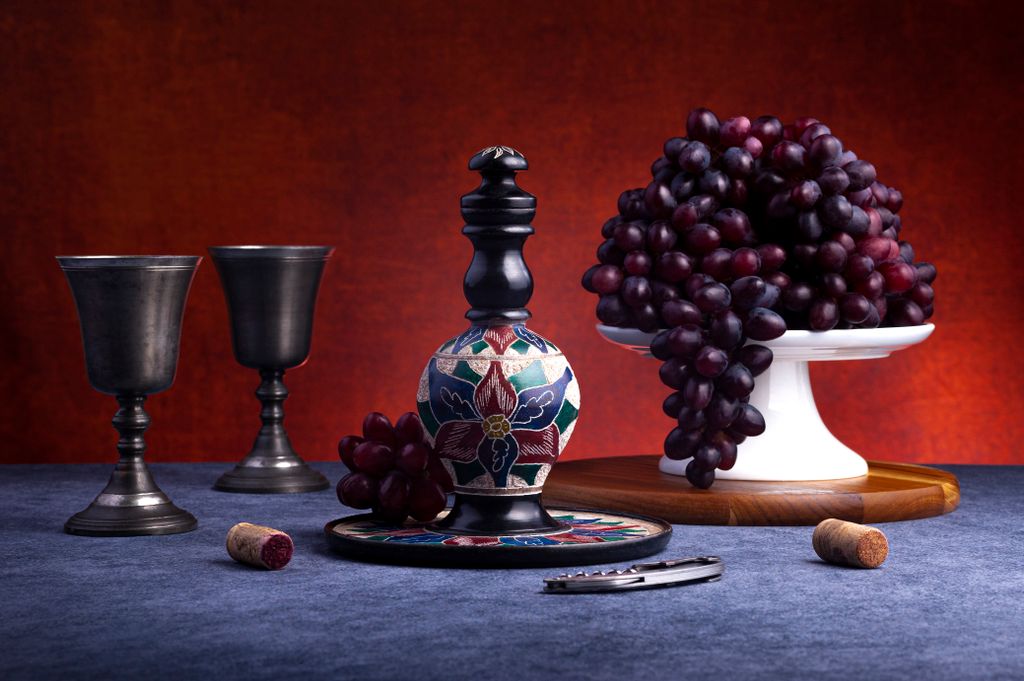 Artistic still life featuring a decorative decanter, grapes, and wine glasses on a table.