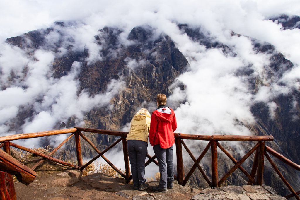 Two hikers admire the stunning view of Colca Canyon under a cloudy sky in Cabanaconde, Arequipa.